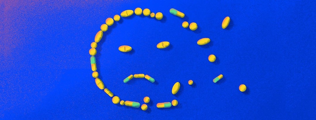 A collection of pills, tablets, and capsules arranged in a sad face. The right-hand side of the pills are scattered rather than in line to create the right of the face.