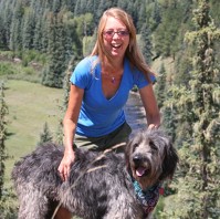 Woman with brown hair and blue shirt with a large, gray shaggy dog.